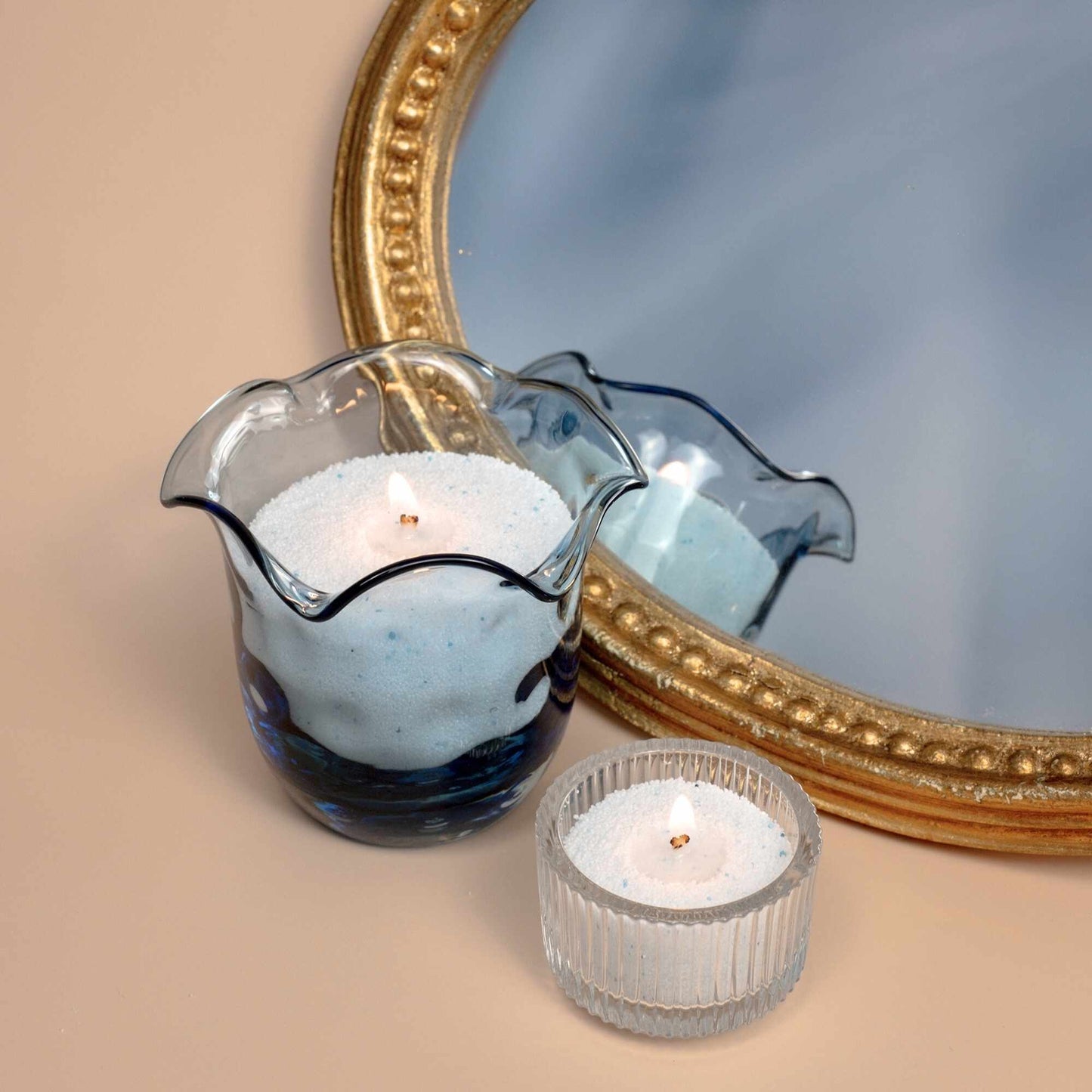 Candles lighting in a blue glass holder and a teacup light, highlighting the versatility of sand candles.