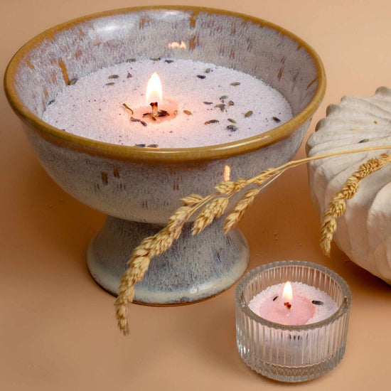Candles lighting in a ceramic holder and a teacup light, highlighting the versatility of sand candles.
