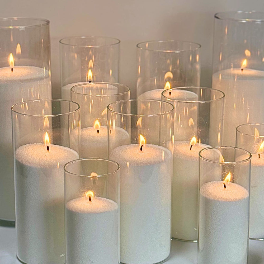 
                      
                        A collection of sand candles made from a 5kg bag of wax, set inside tall, clear glass cylinders of varying sizes, with each candle emitting a warm flame, showcasing the product's capacity for creating multiple candles.
                      
                    