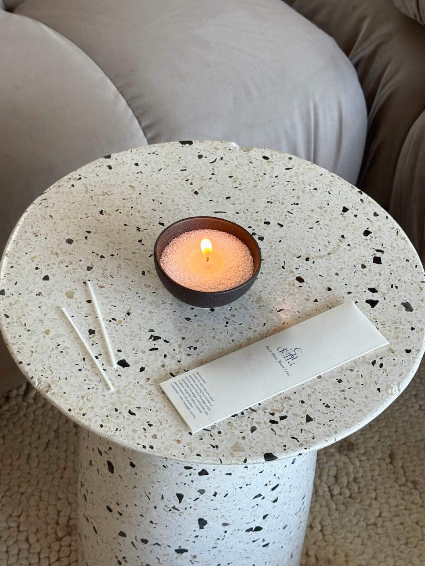 A sand candle lit on a coffee table with a candella wick bag beside it.