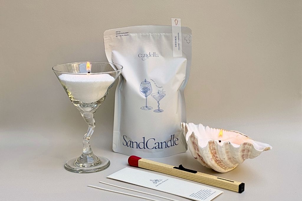 A classic-sized sand candle with a matchstick lighter and wick pouch, surrounded by a seashell martini and seashell lighting, all using sand candles.