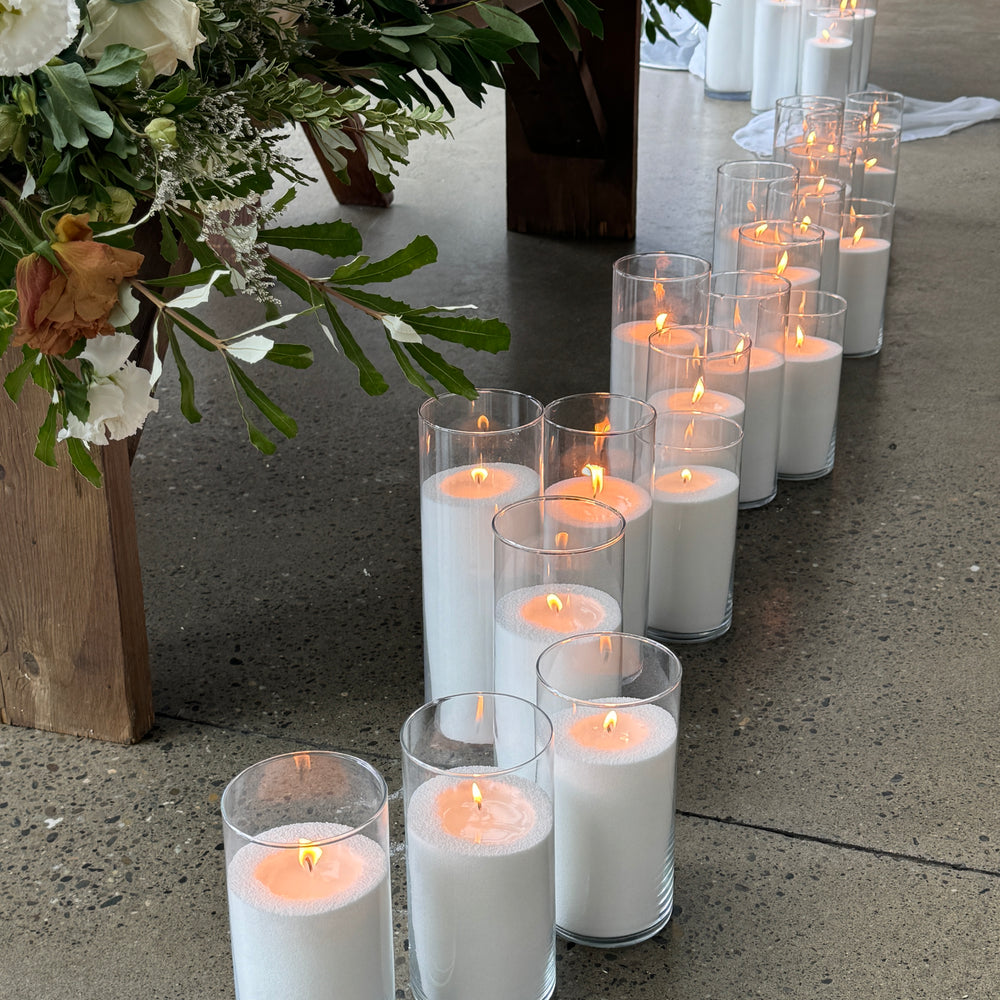 A row of glass vessels with lit candella sand candles, creating a romantic ambiance.