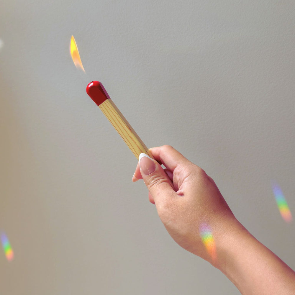 A hand holding the matchstick lighter with the flame on.