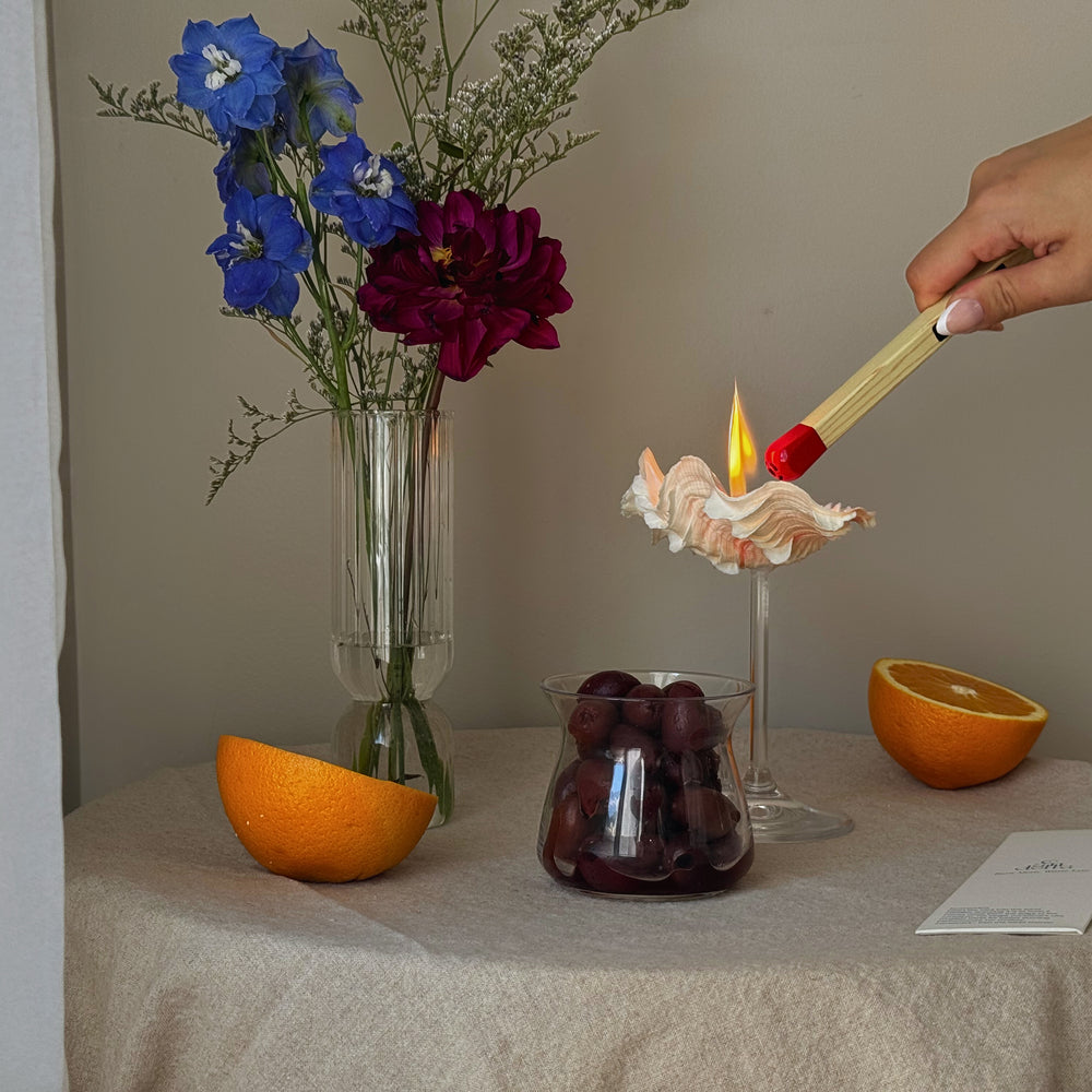 A matchstick lighter lighting a candle in a seashell martini glass made by sand candles from candella.