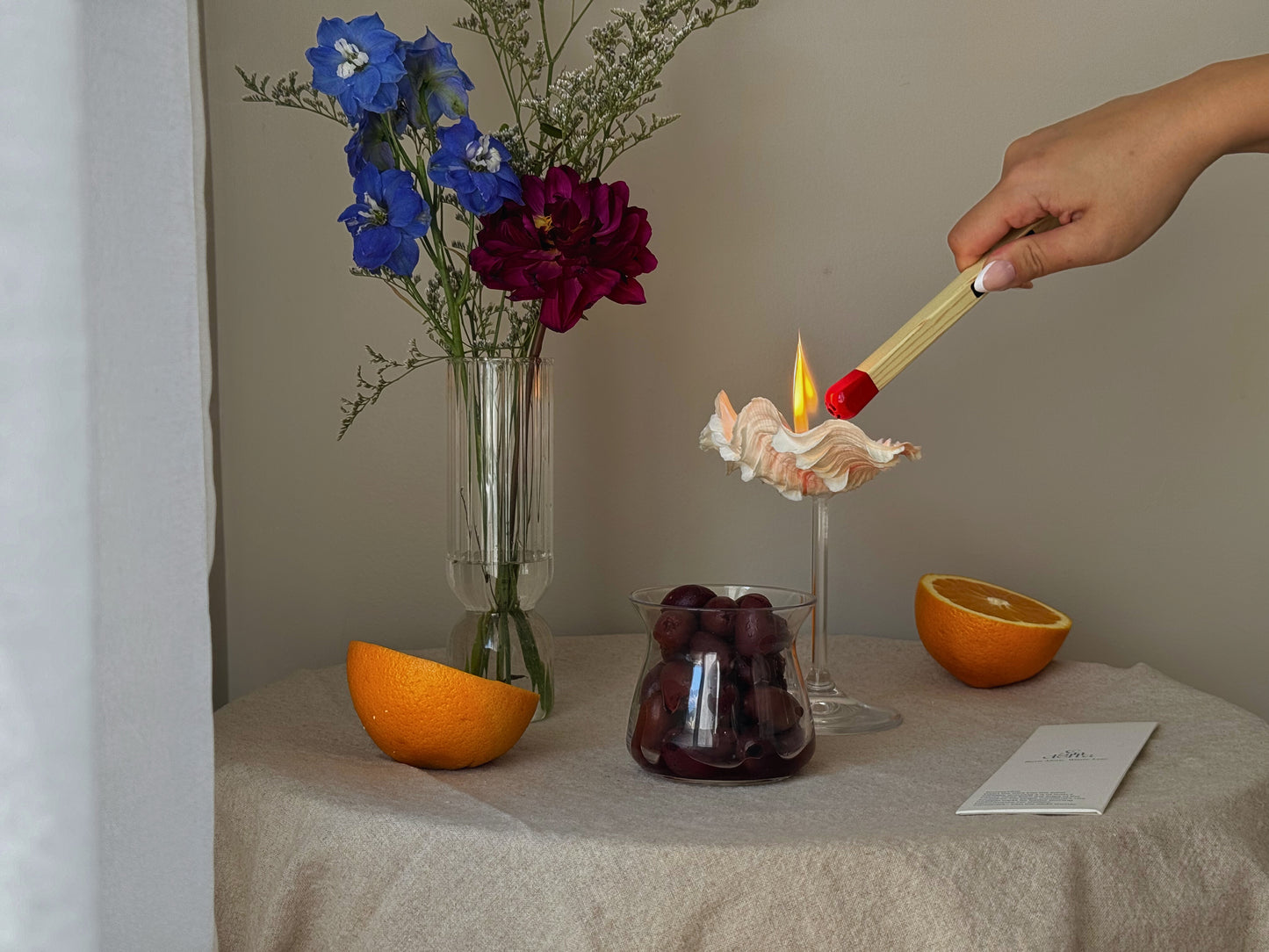 A matchstick lighter lighting a candle in a seashell martini glass made by sand candles from candella.