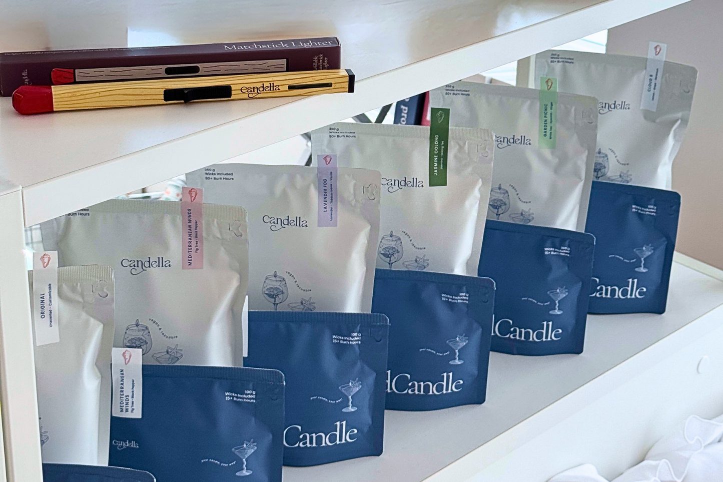 Collection of Candlella product packages on a white surface with books in the background.