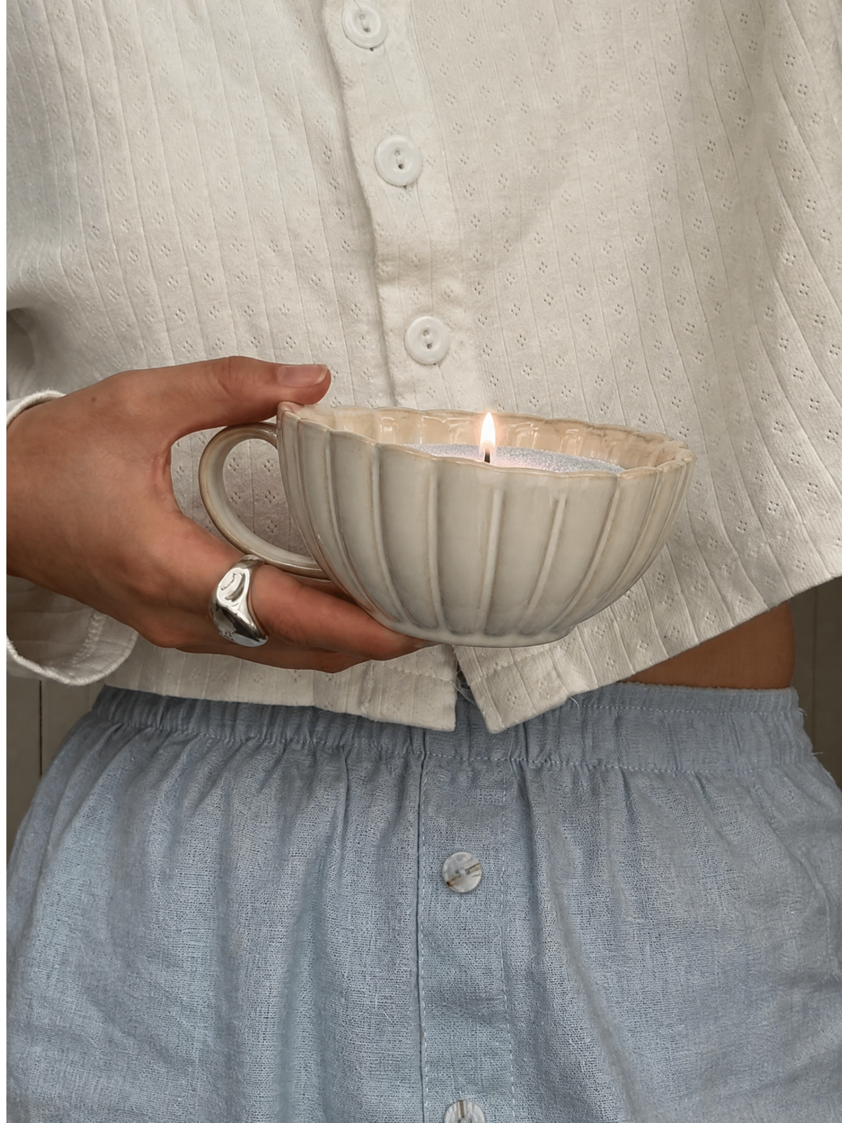 A person holding a lit Cloud 9 sand candle in a wide, ribbed ceramic cup