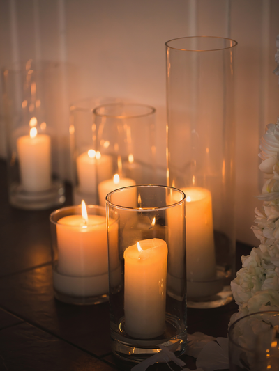 Candlelit scene with various candles in glass holders on a reflective surface.