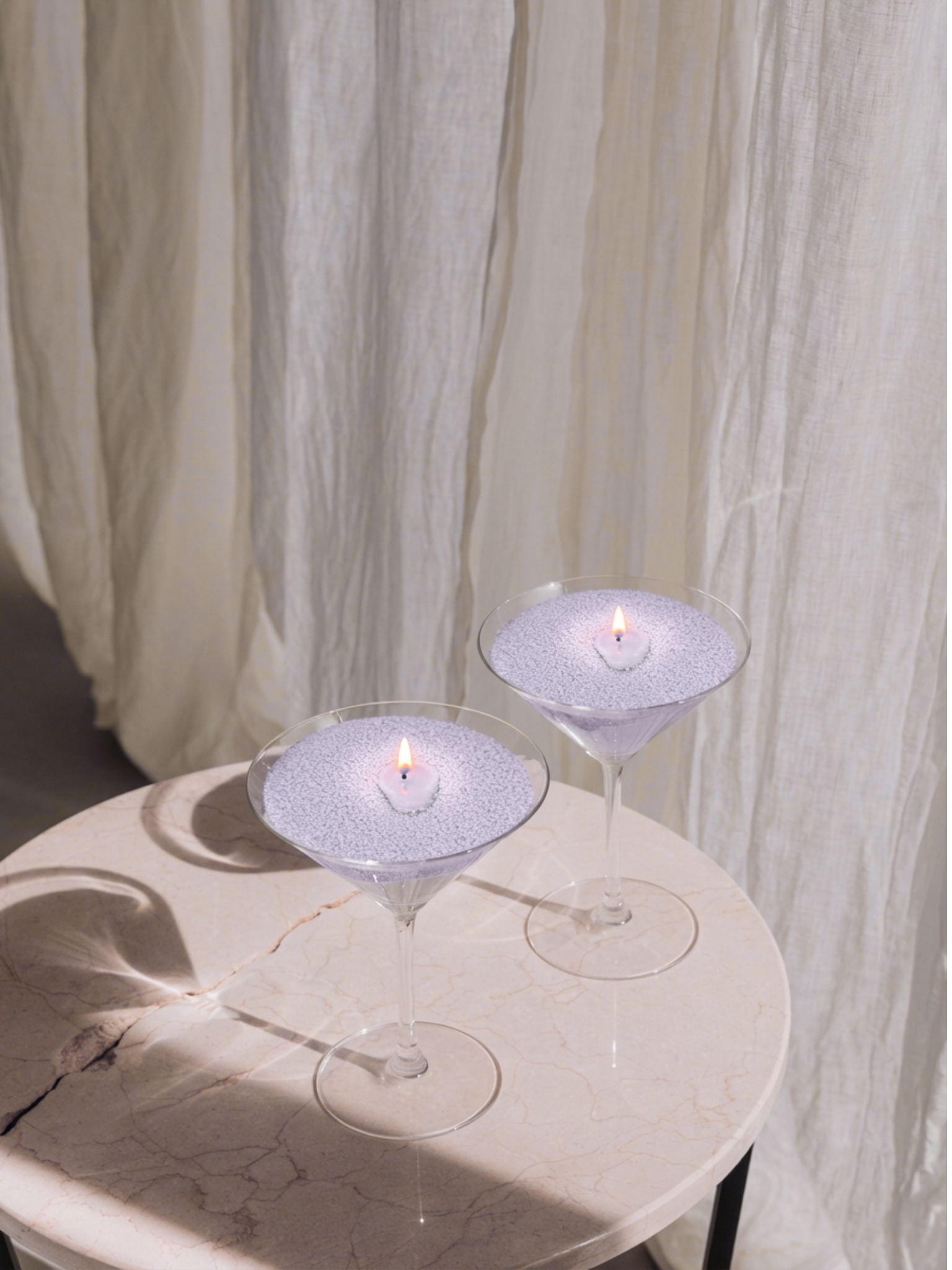 Lit Candella Lavender Fog sand candles in martini glasses on a marble table